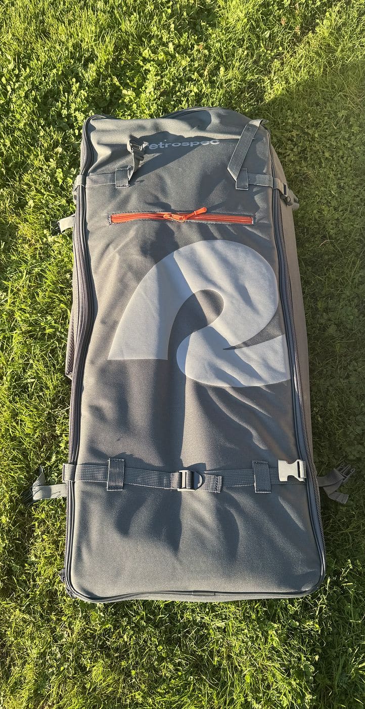 Front of the gray Retrospec paddleboard backpack lying on grass with its large R logo, orange zipper pull and compression straps