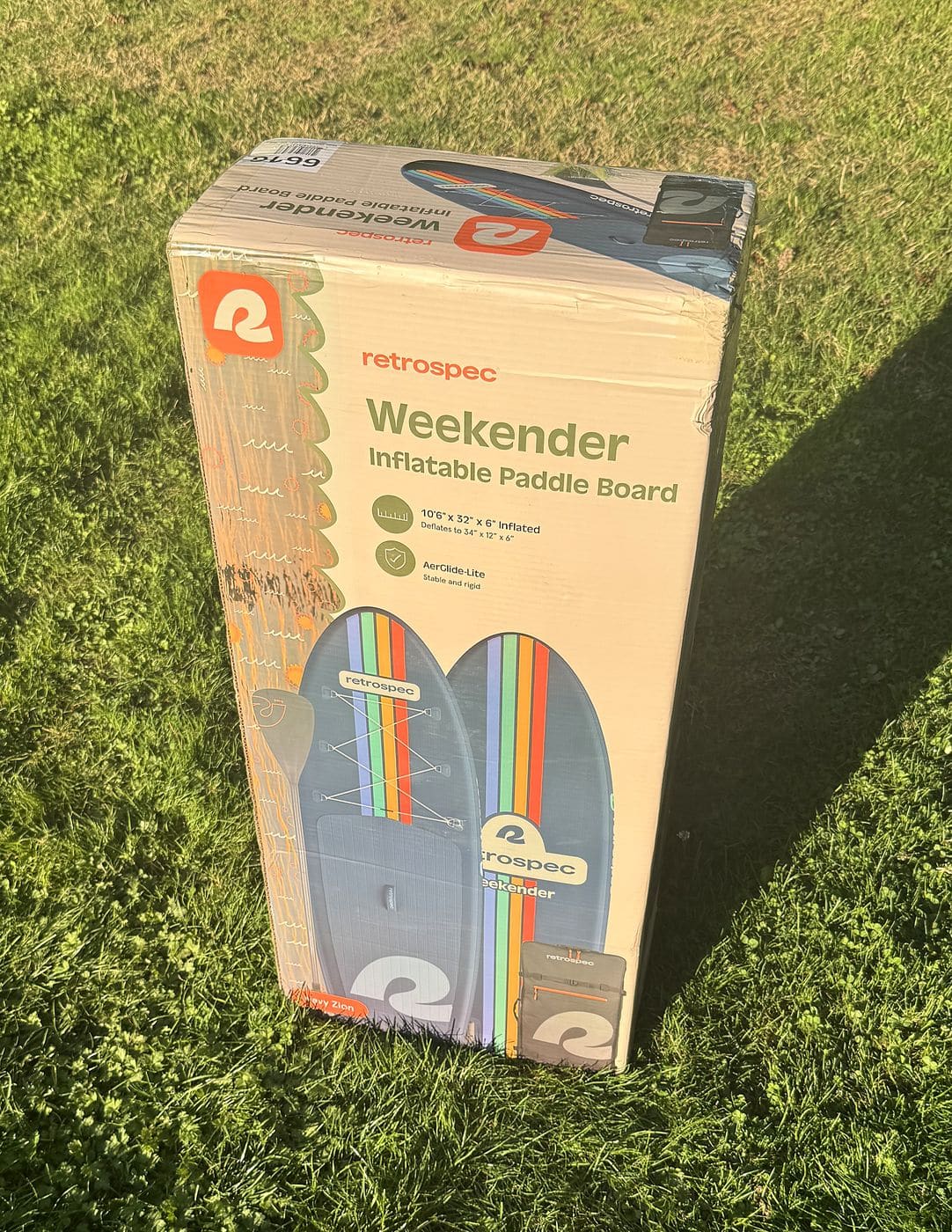Retrospec Weekender inflatable paddleboard retail box standing upright on a lawn