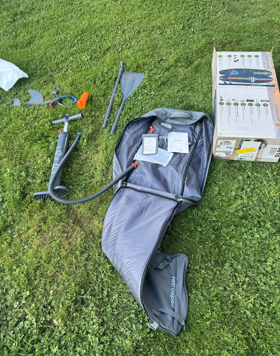 All Weekender components laid out on the grass, including the backpack, pump, paddle, fins, leash and repair kit canister