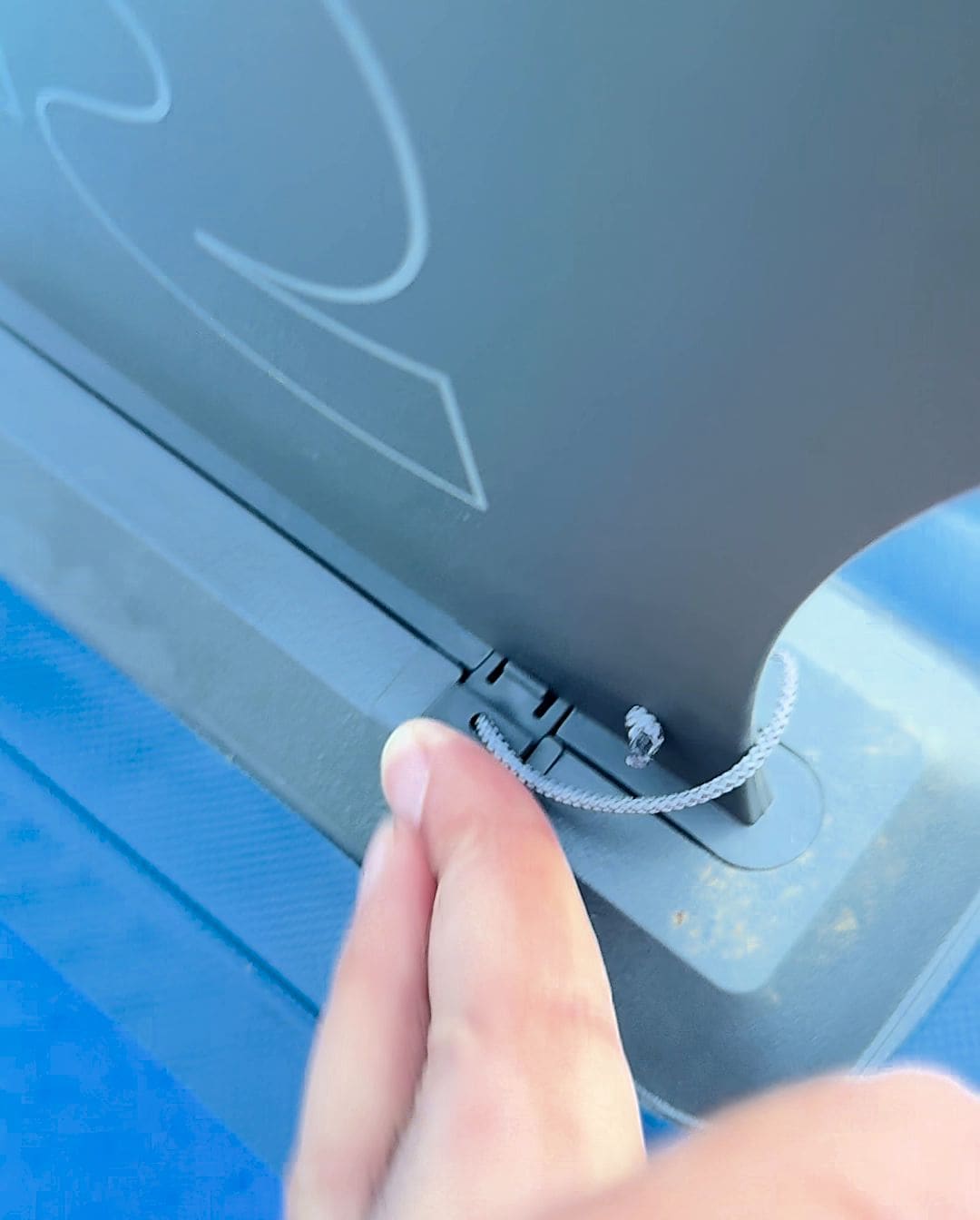 Close-up of fingers inserting the tethered locking pin into the base of a Retrospec slide-in fin