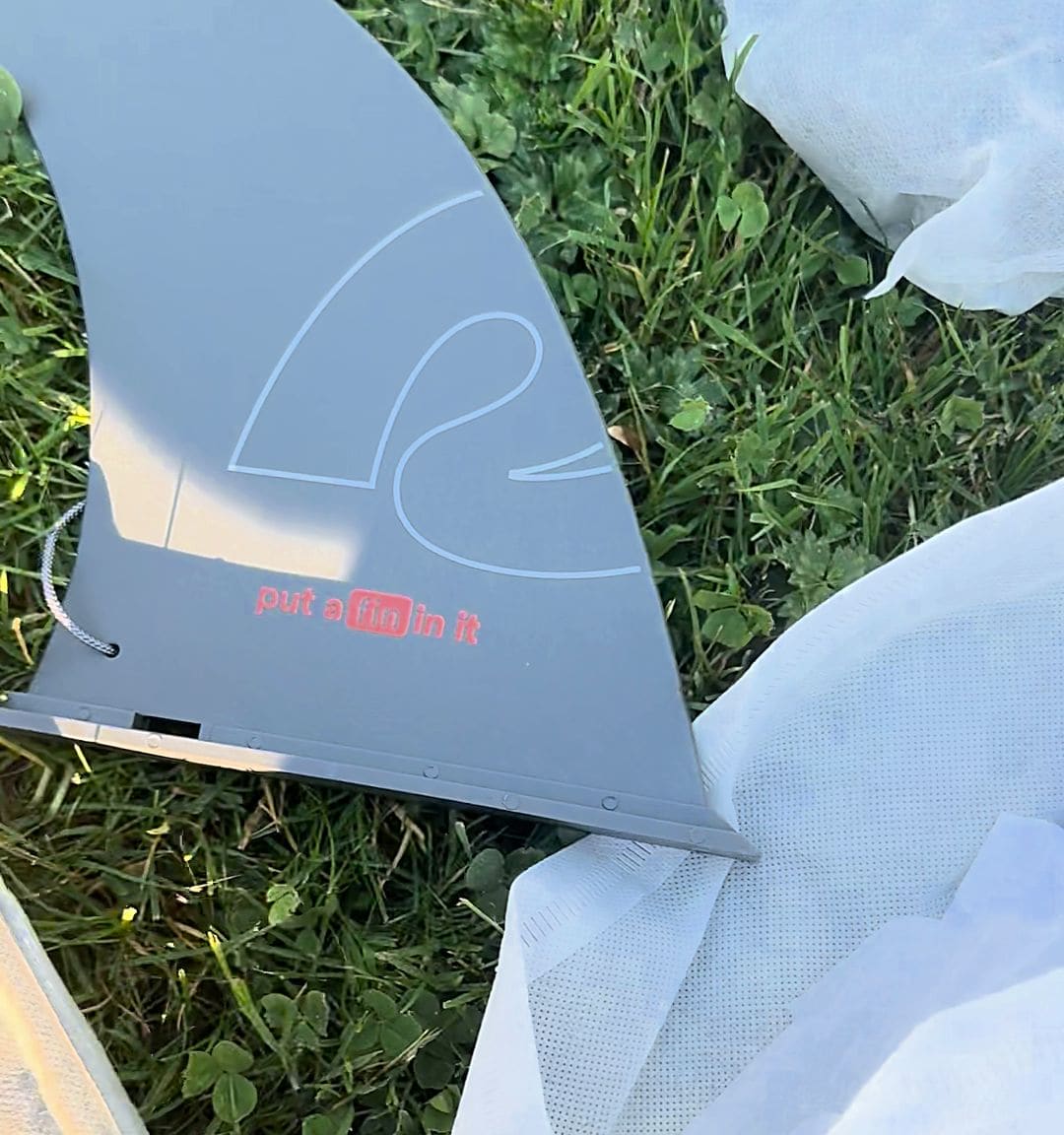 Gray Retrospec center fin on the grass printed with the slogan put a fin in it