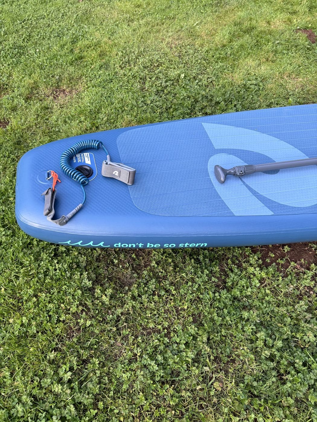 Tail of the Weekender on grass showing the printed rail text reading don't be so stern next to the leash and paddle